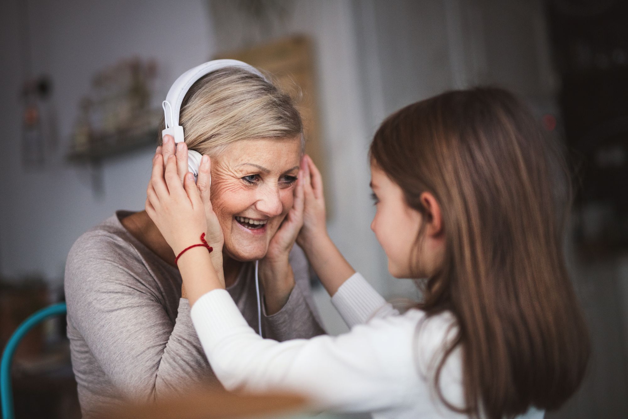 Granddaughter placing headphones on smiling grandmother as they share a song together