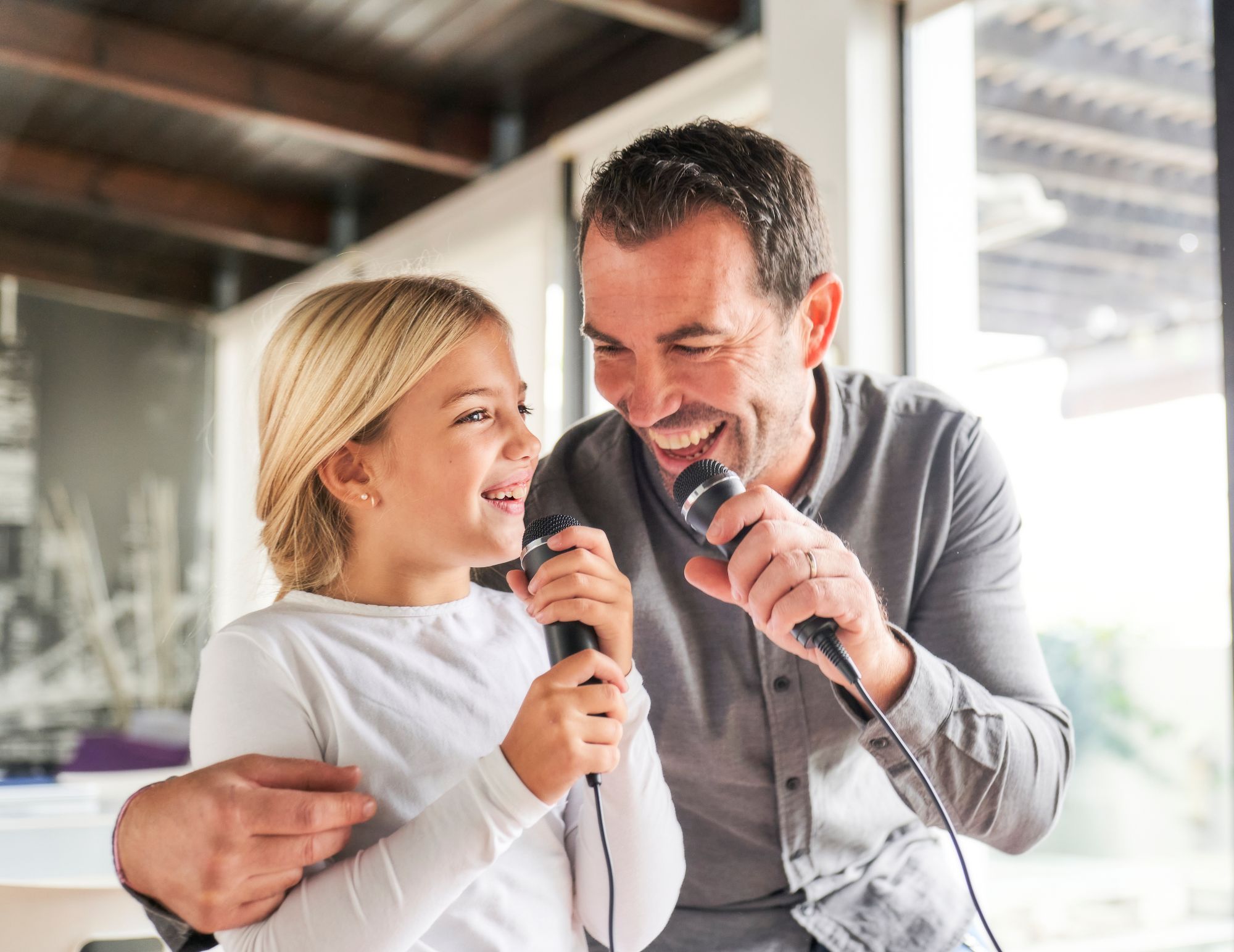 Dad and young daughter laughing and singing together into microphones at home