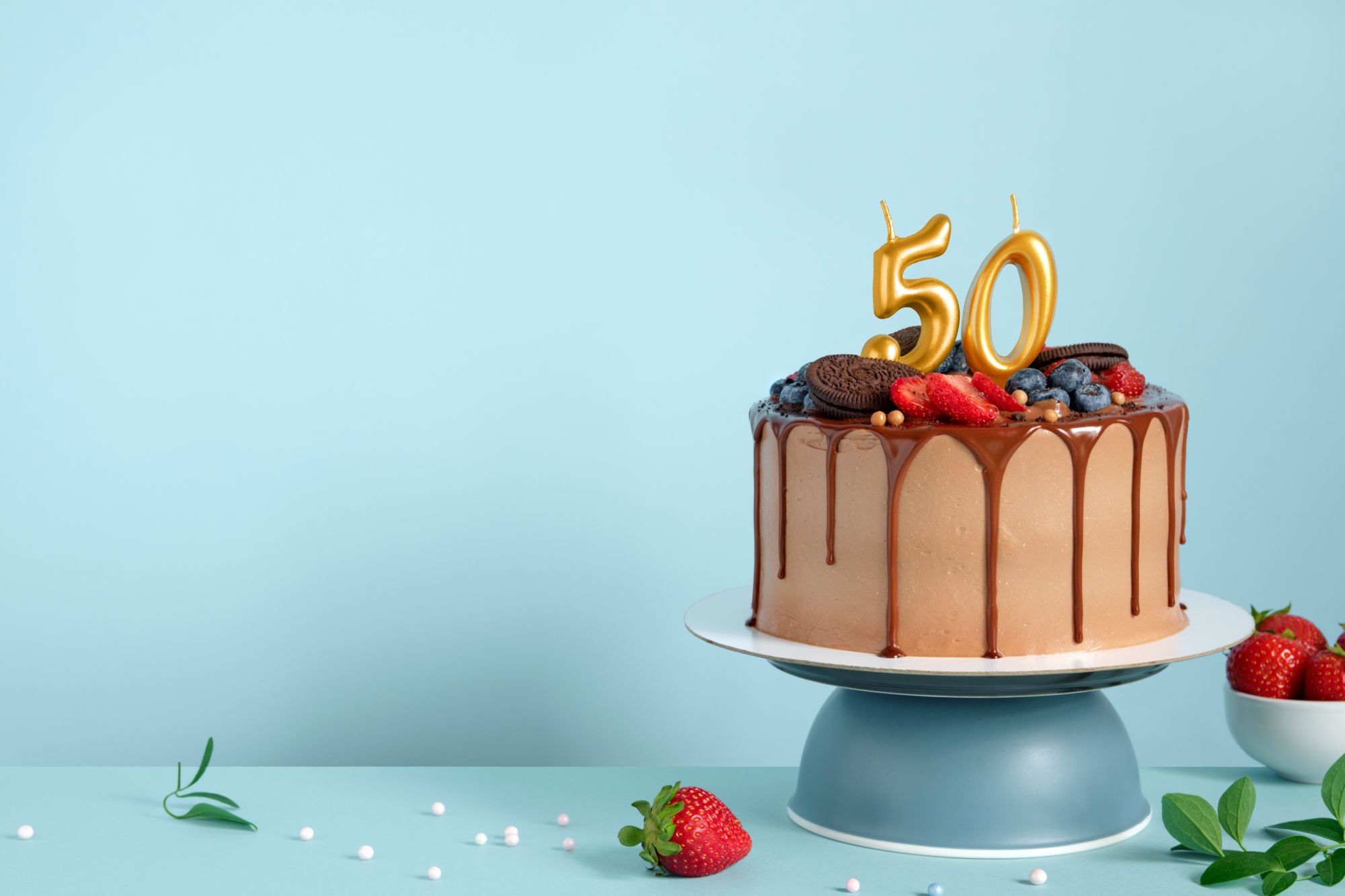 Chocolate drip birthday cake topped with gold 50 candles, berries and strawberries