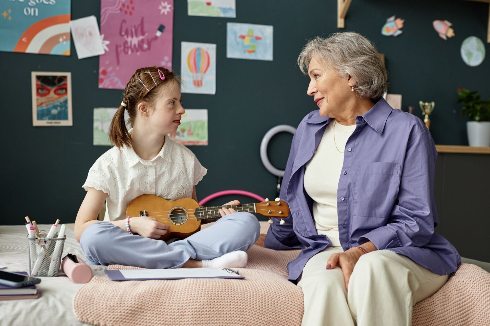 Young girl playing ukulele for her grandmother in a cozy bedroom