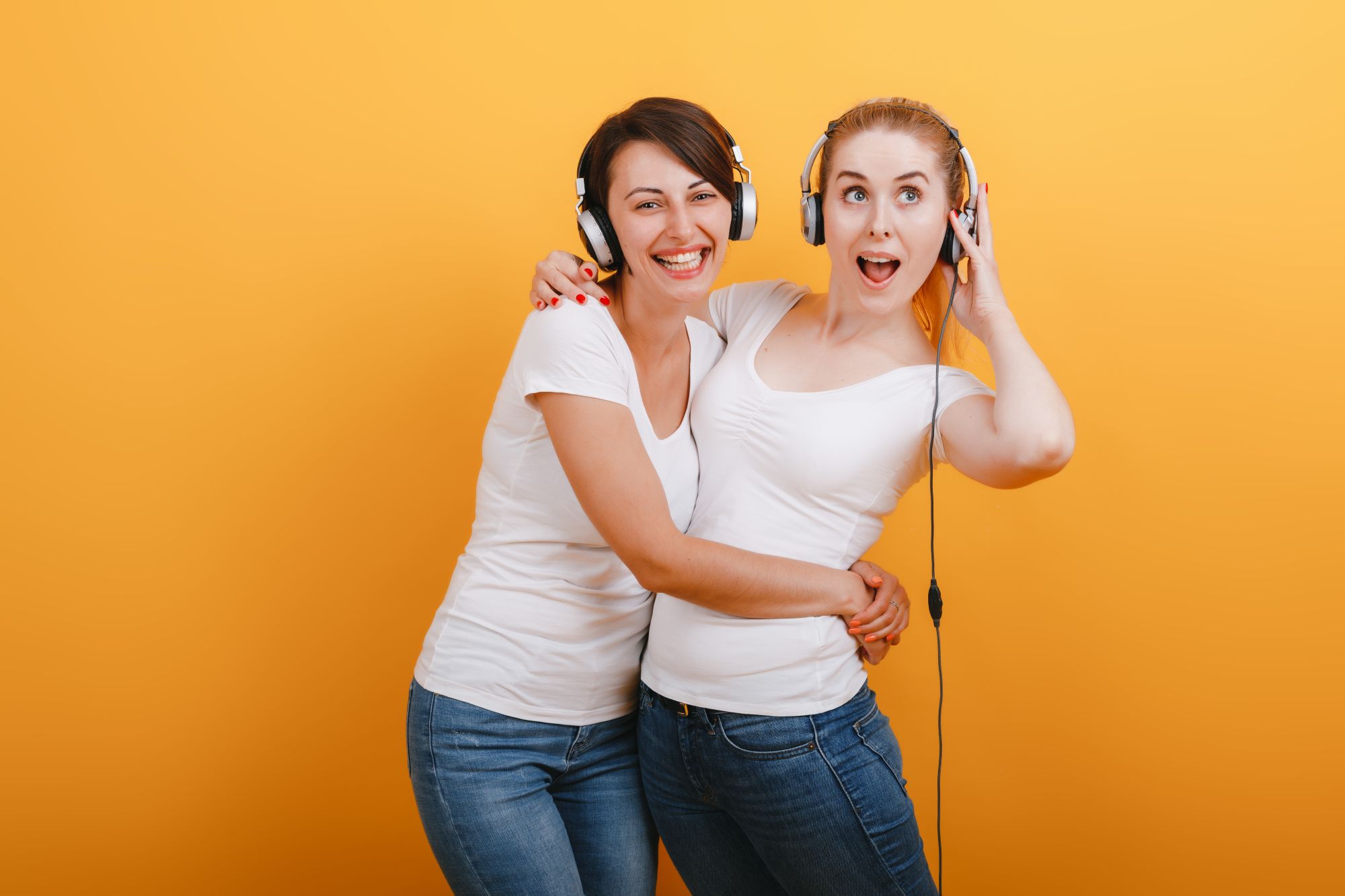 Two sisters hugging and dancing with headphones on a bright yellow background