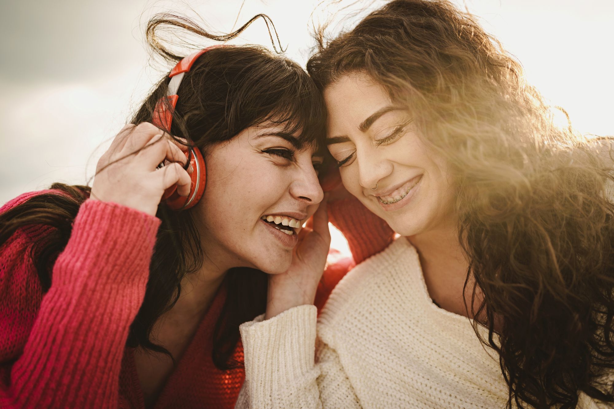 Two sisters laughing together while sharing headphones in golden sunlight