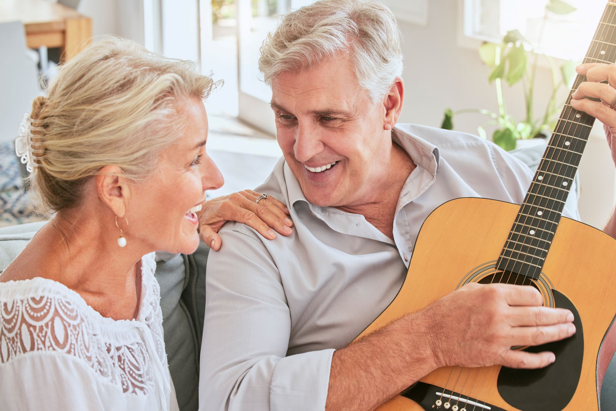Older couple smiling together as the husband plays acoustic guitar