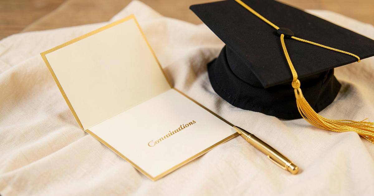 Open cream congratulations card with gold edging beside a graduation cap and gold pen