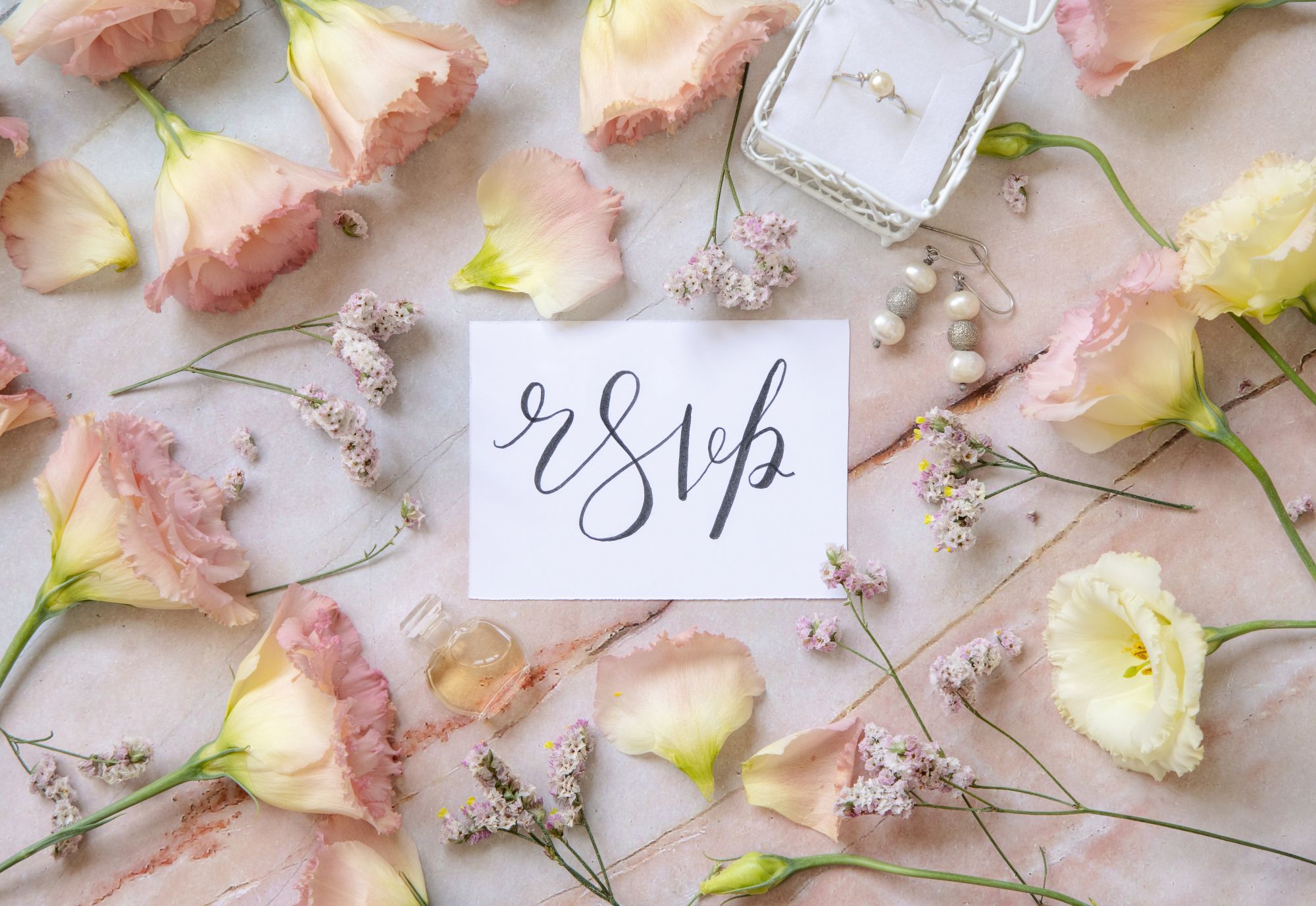 Hand-lettered RSVP card surrounded by pastel flowers and pearl jewellery