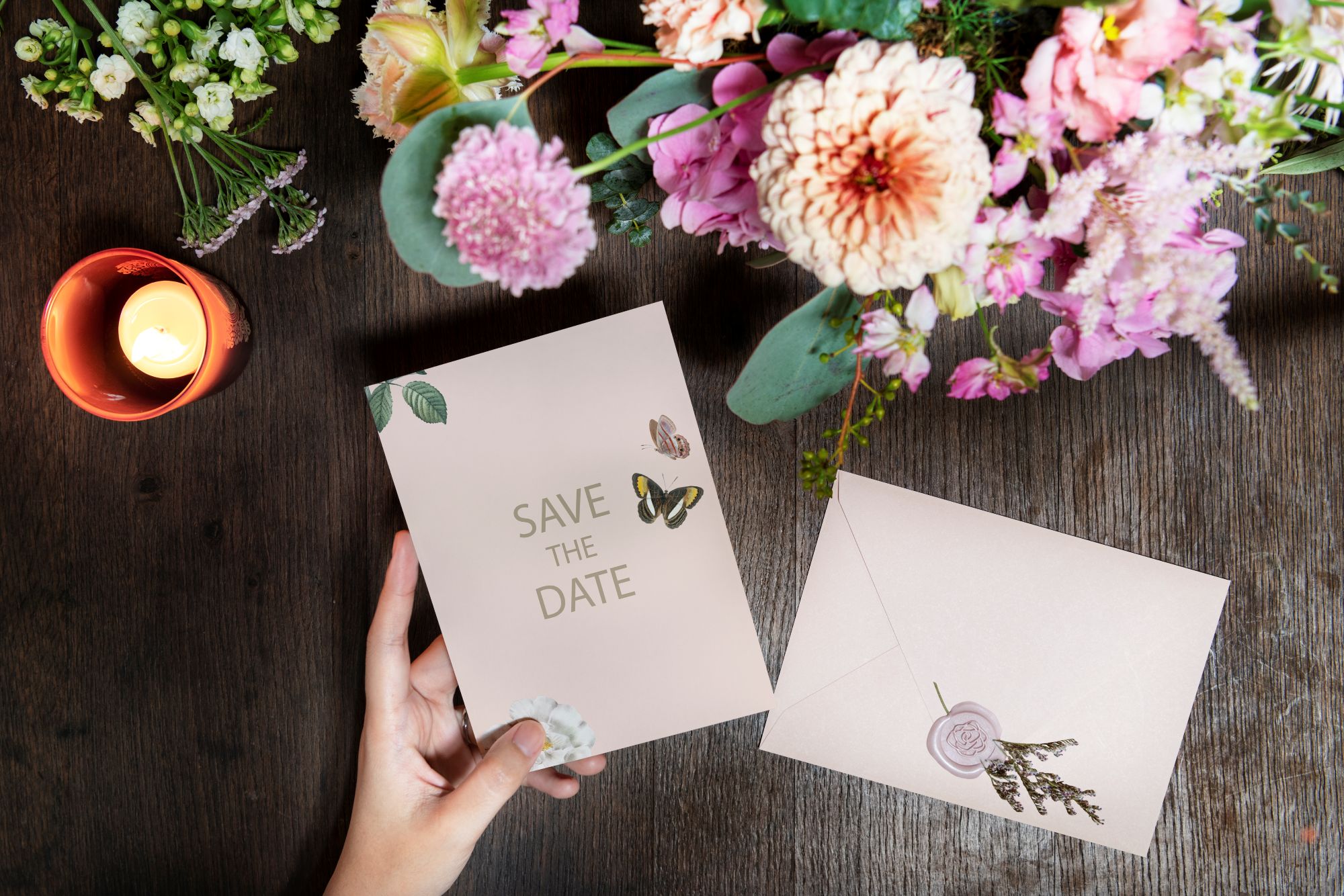 Pink Save the Date invitation card held over a wooden table with floral bouquet