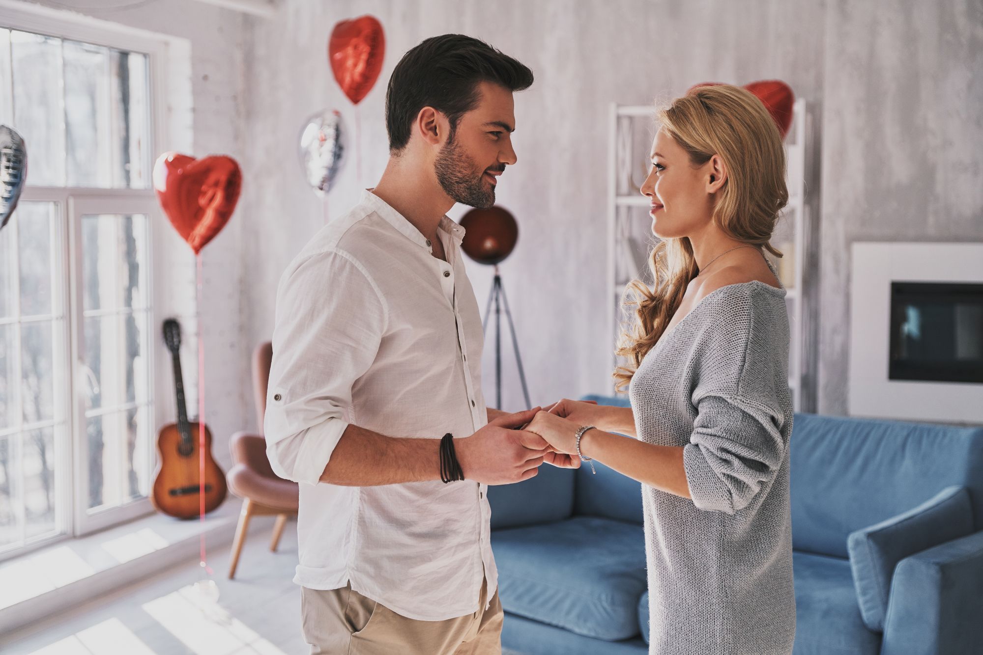 Young couple holding hands and dancing with red heart balloons in the background