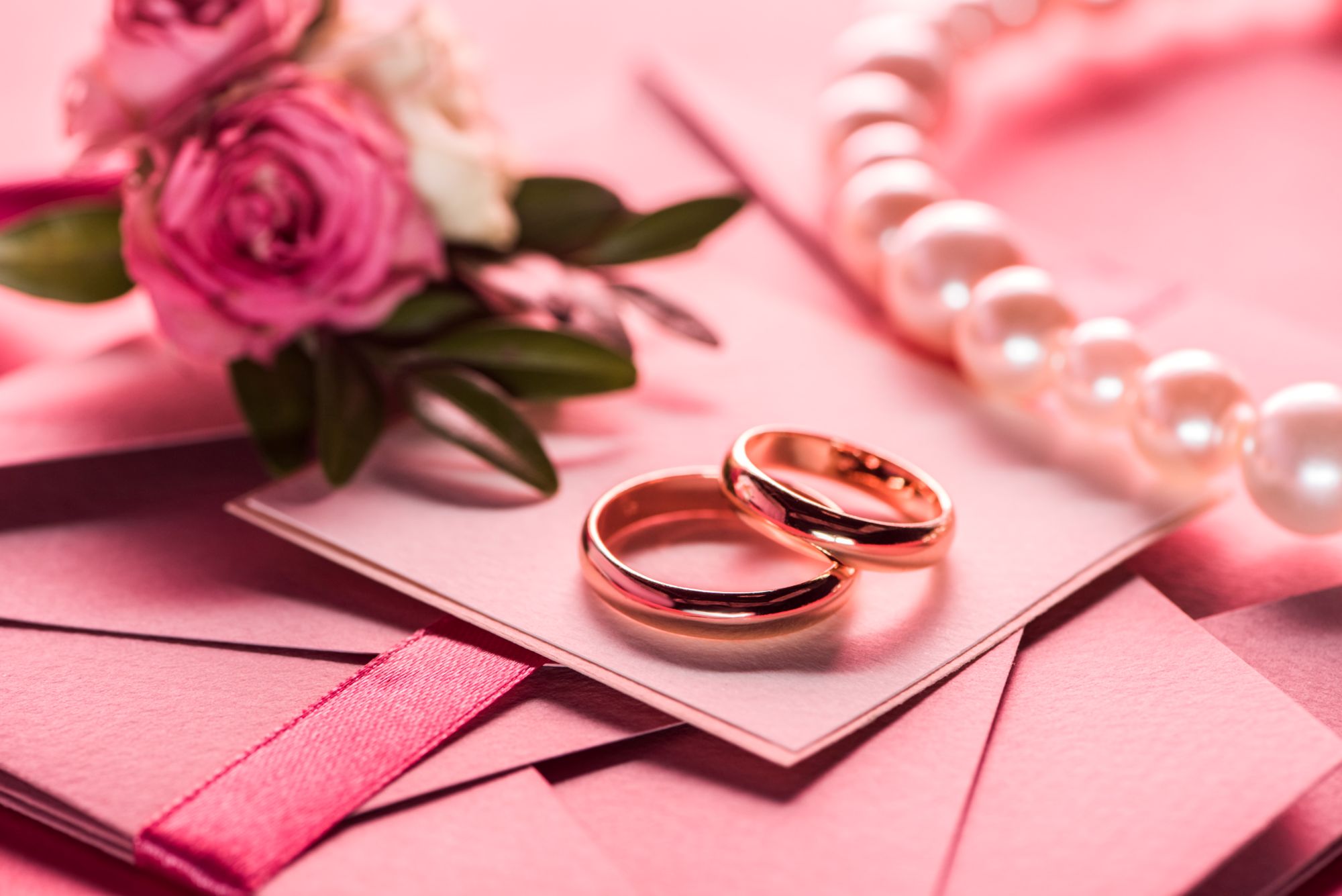 Two gold wedding rings on pink stationery with roses and pearls