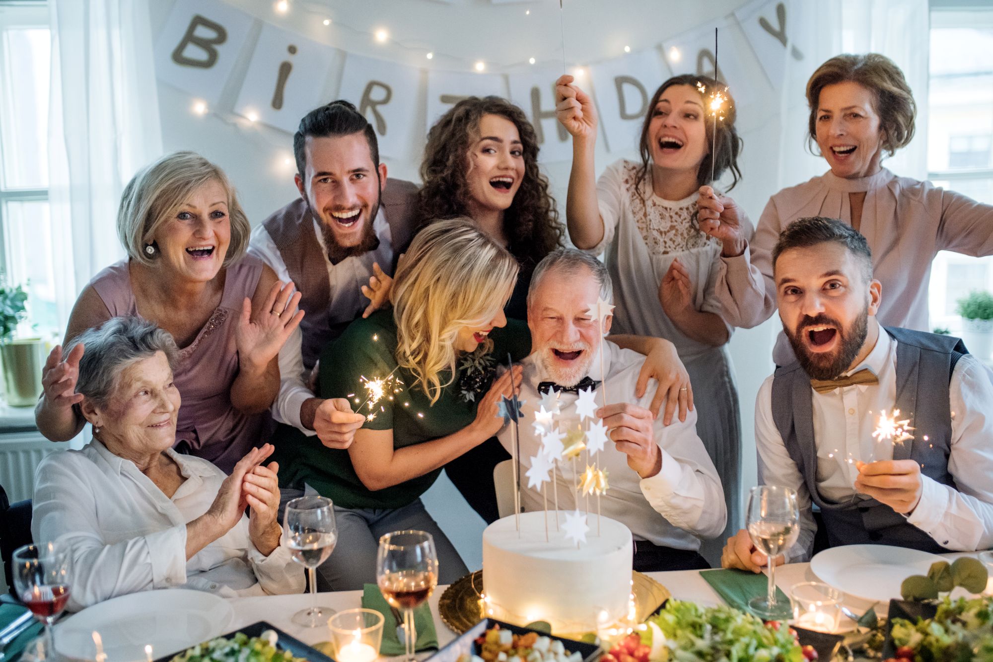 Multi-generational family around a birthday cake with sparklers, listening to a personalised birthday song that says grandad's name