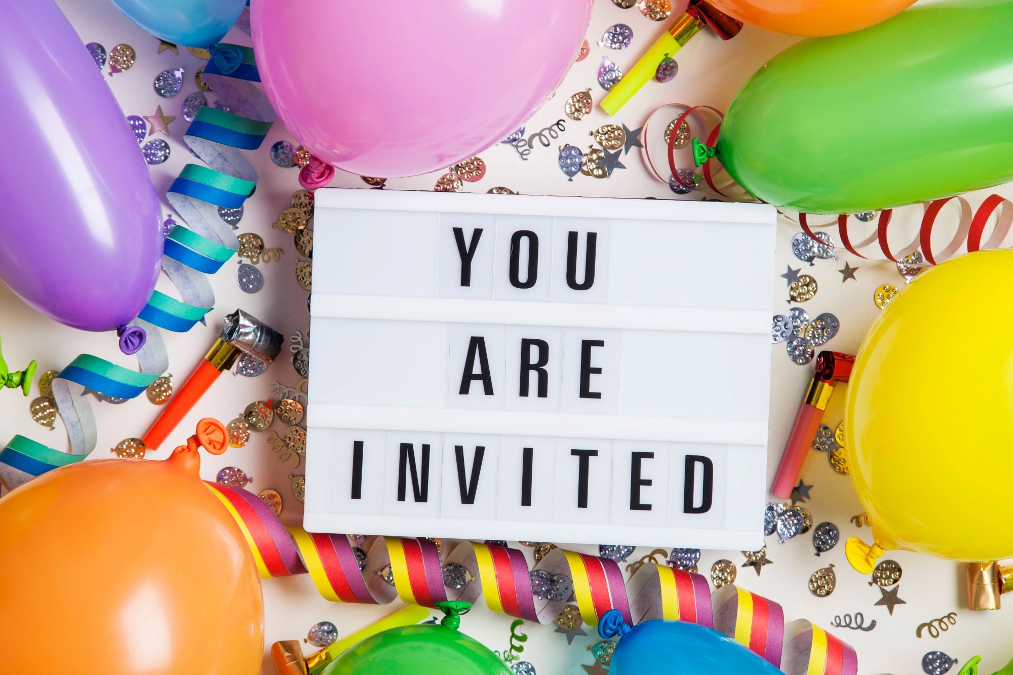 You are invited lightbox sign surrounded by colourful balloons and confetti